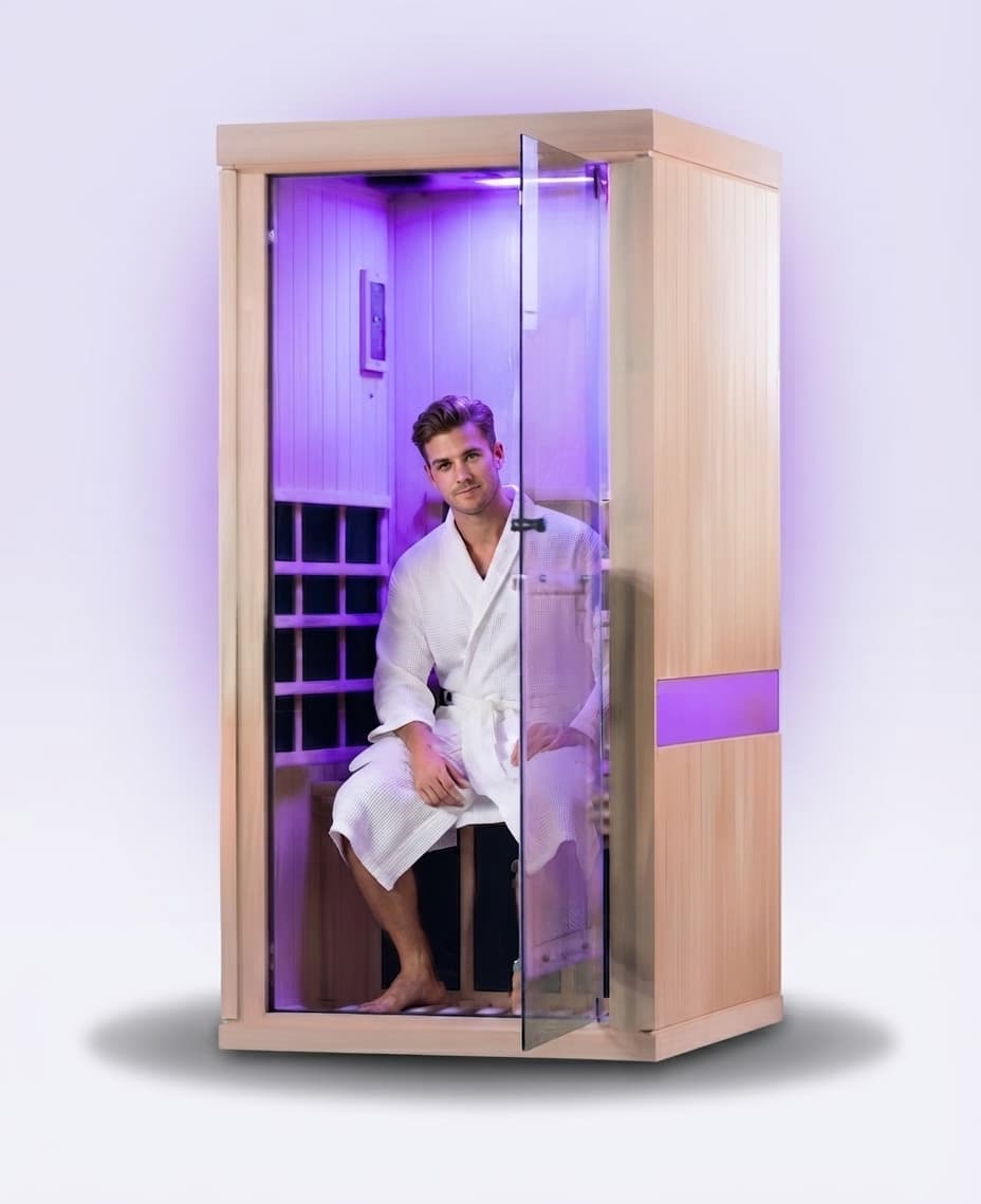A relaxed man in a white robe seated inside a private Cappa sauna cubicle glowing with soft purple light